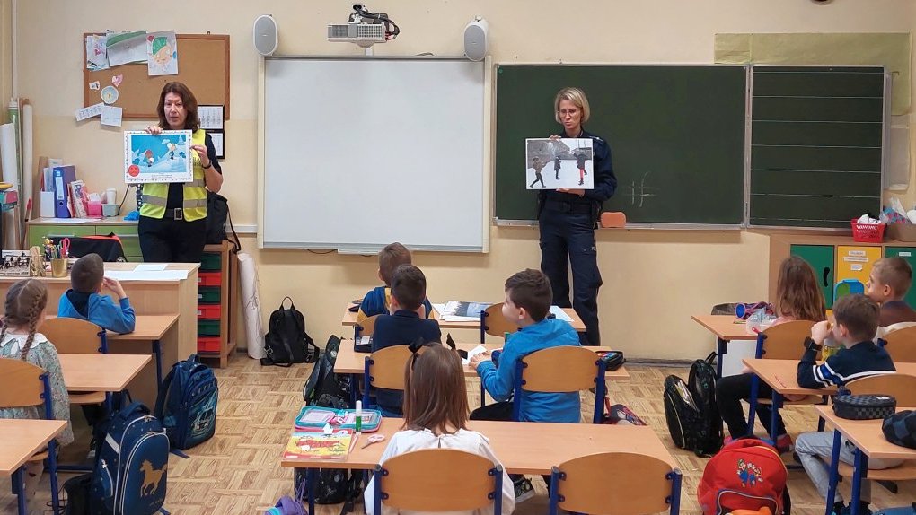 strażniczka wraz z policjantką przedstawiają sytuacje na planszach i rozmawiają z uczniami o bezpiecznym uczestniczeniu w zimowych zabawach