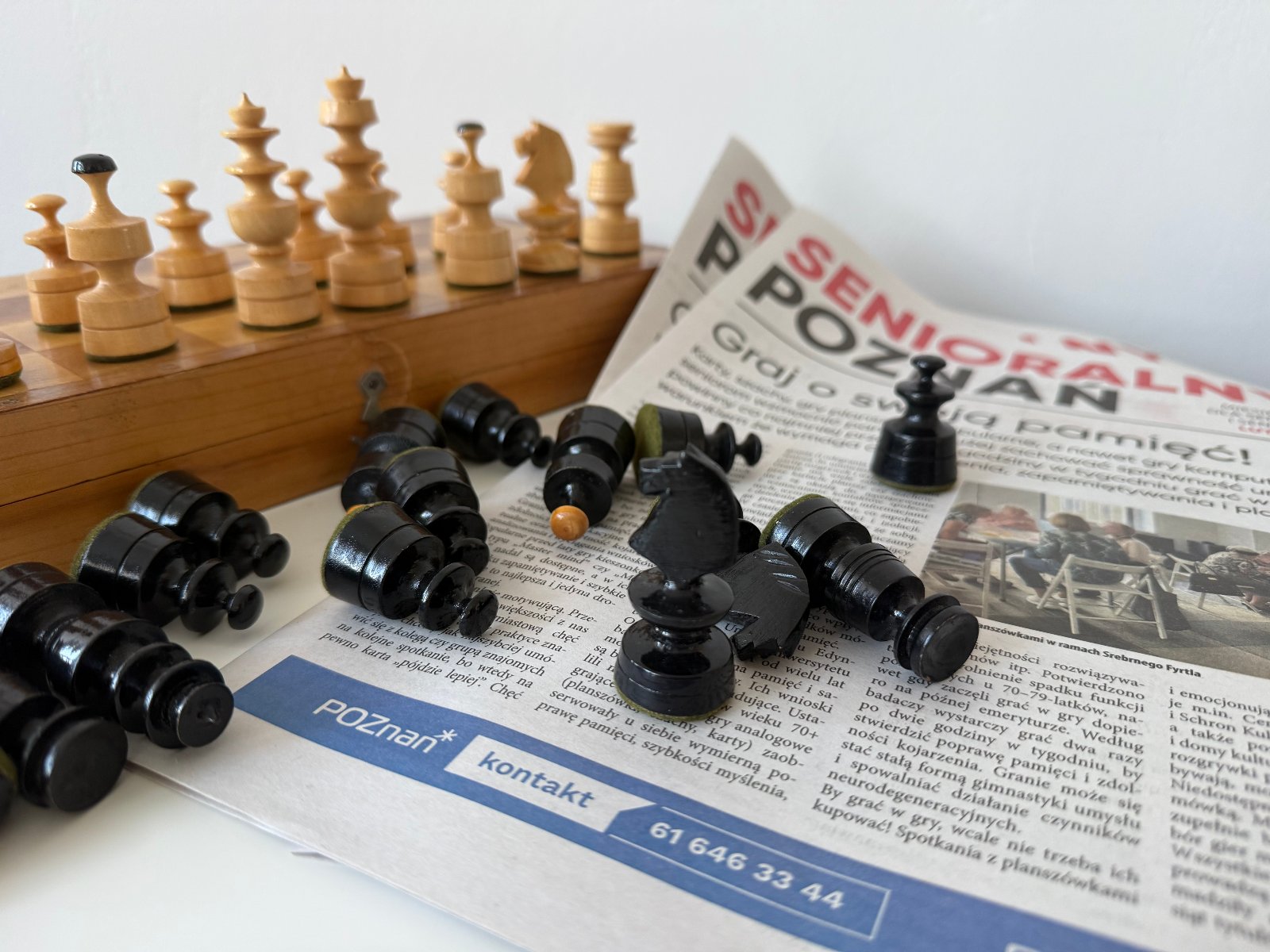Zdjęcie przedstawia gazetę Senioralny Poznań oraz drewniane szachy