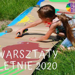 Dziwczyna maluje słońce i zwierzęta na szrym papierze rozłozonym na trawie.