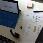 Laptop na stole, obok słuchawki, kartki, tablet, pisaki.