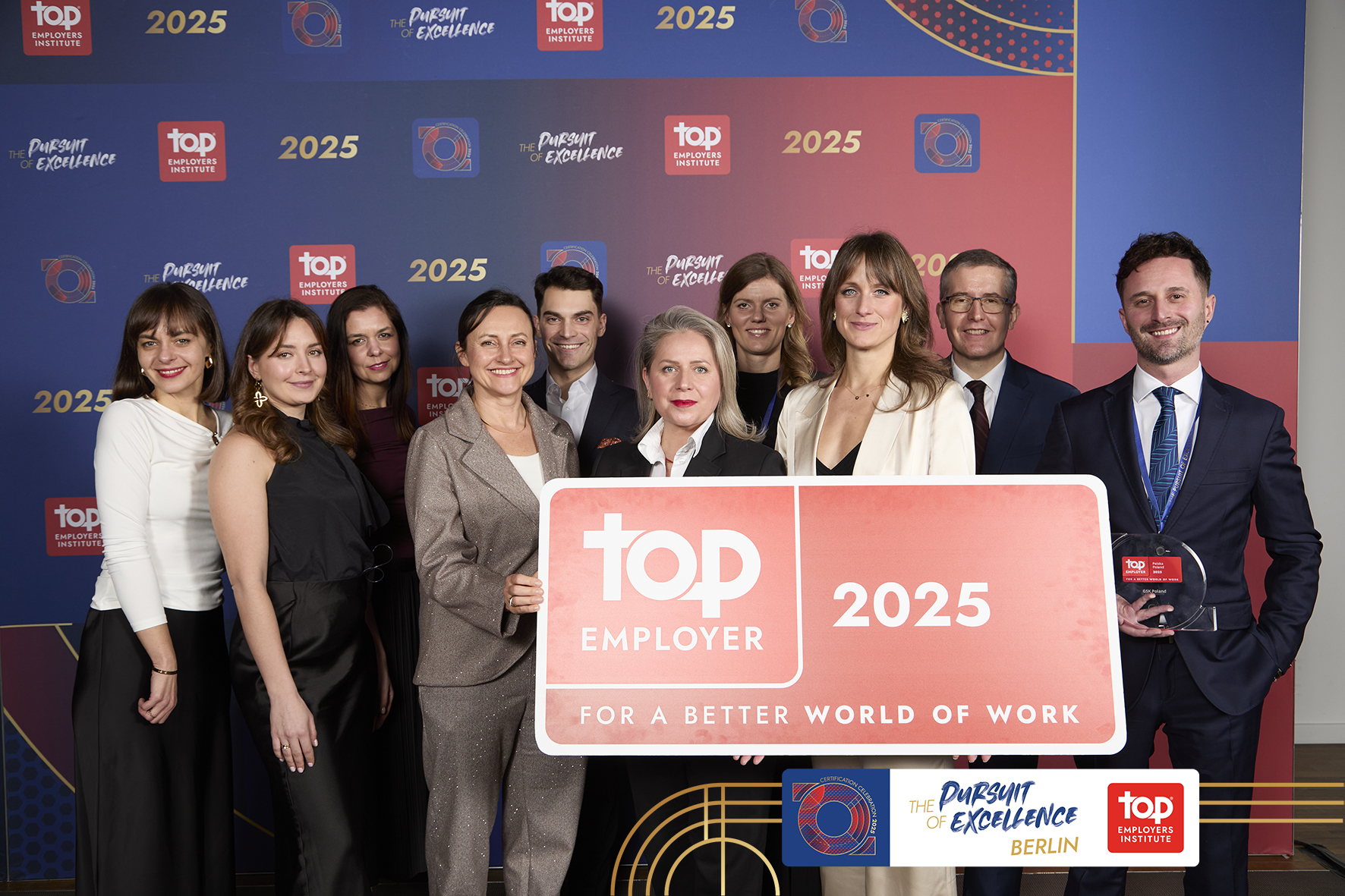 A group of people dressed in elegant outfits. They pose with the Top Employer 2025 award statuette.