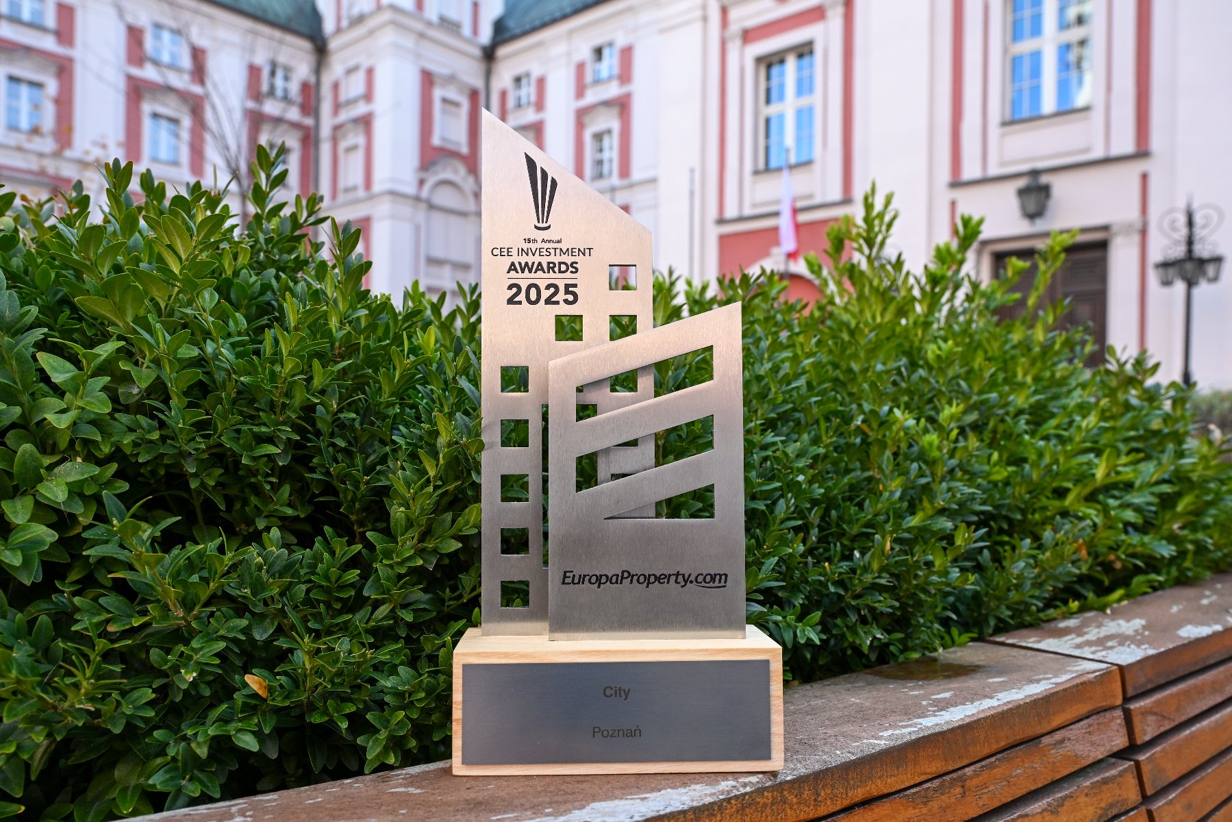 A metal award depicting two intersecting skyscrapers. In the background, vegetation and the City Hall building.