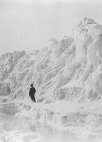 The black-and-white photograph shows a man standing in front of a great snowdrift.
