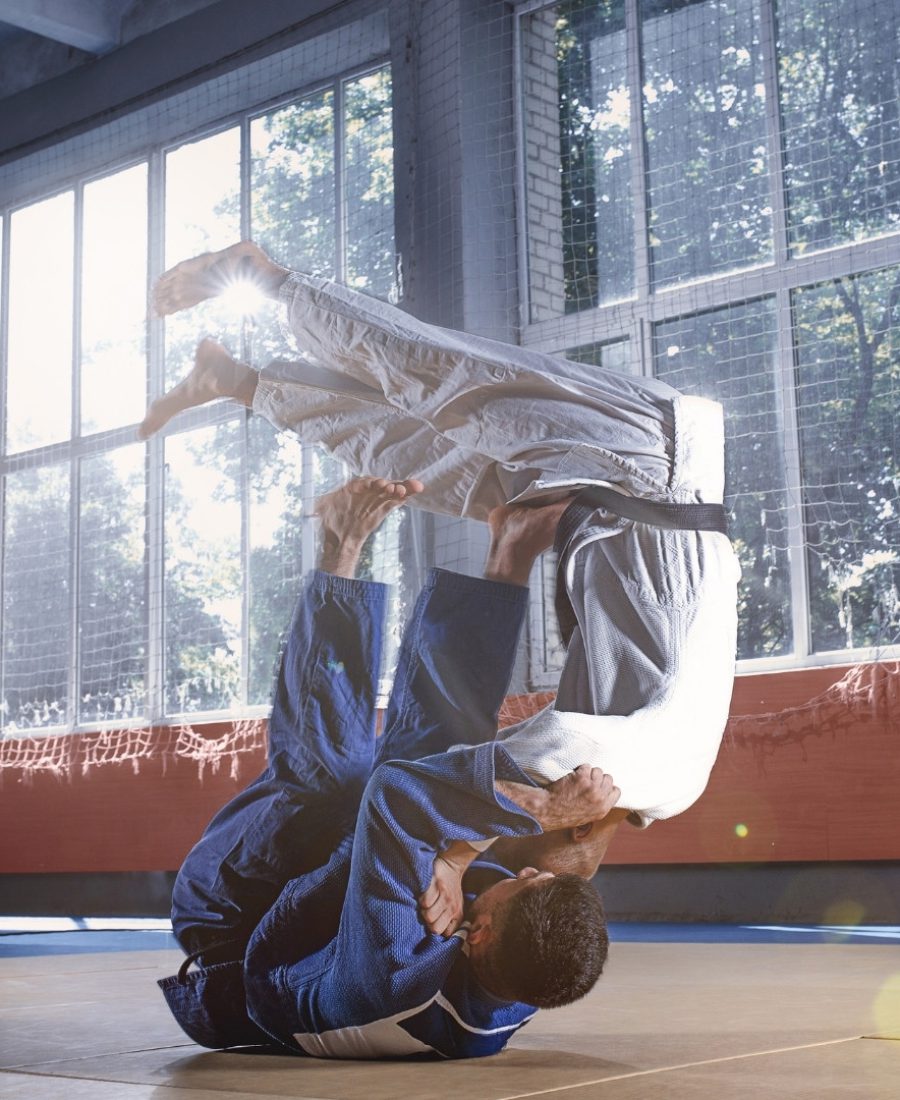 Zawodnicy ubrani w białą i niebieską judogę ćwiczą judo na macie