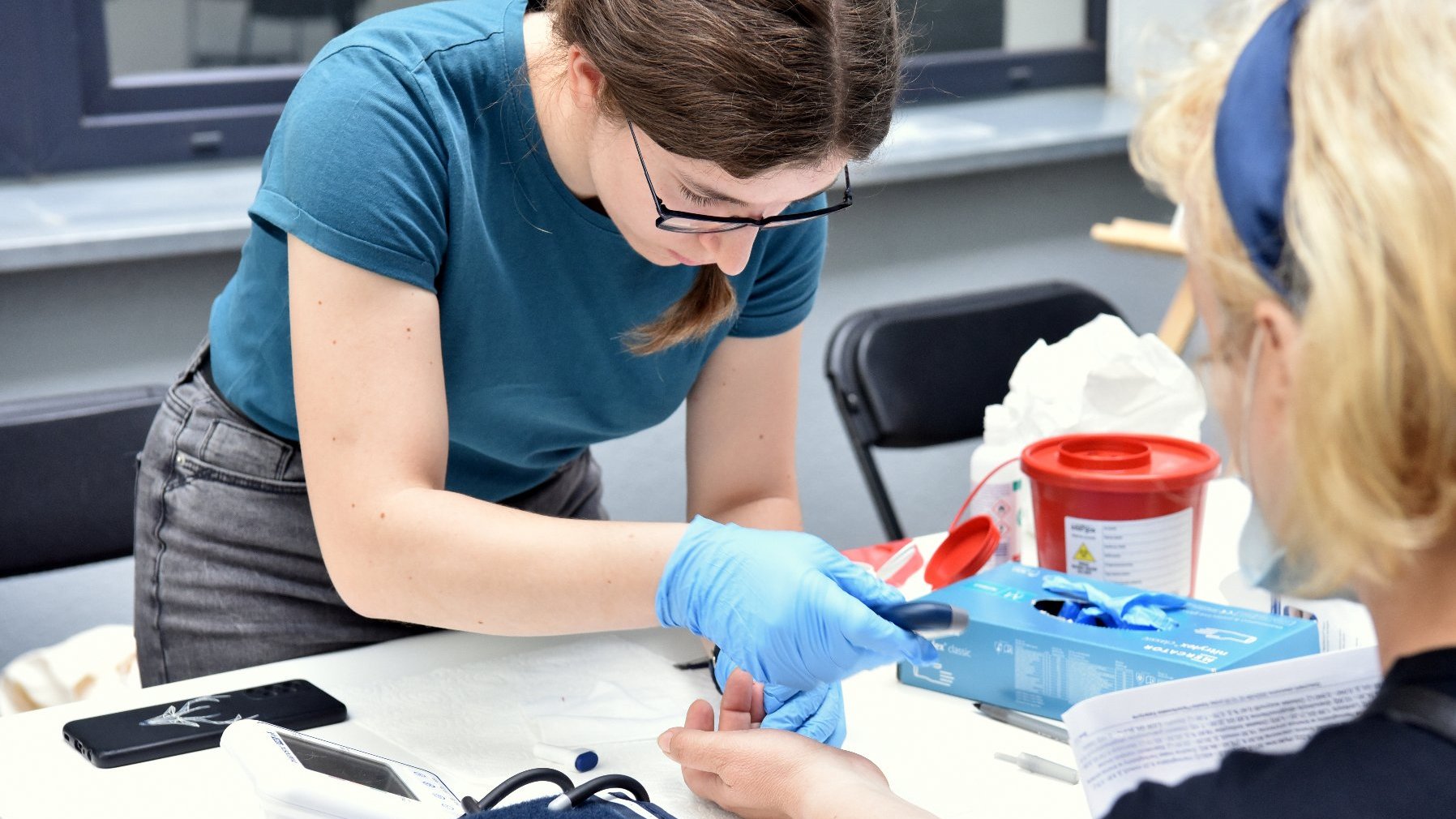 Osoba w rękawiczkach przeprowadza badanie krwi.