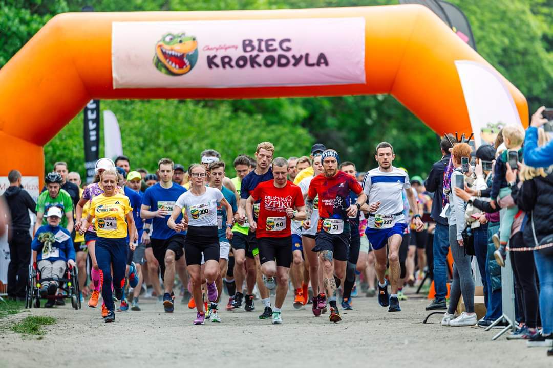 Bieg Krokodyla 2024 - kilkadziesiąt osób rozpoczyna start biegu. W tle widać pomarańczową bramę pneumatyczną, a z boku dopingujących kibiców