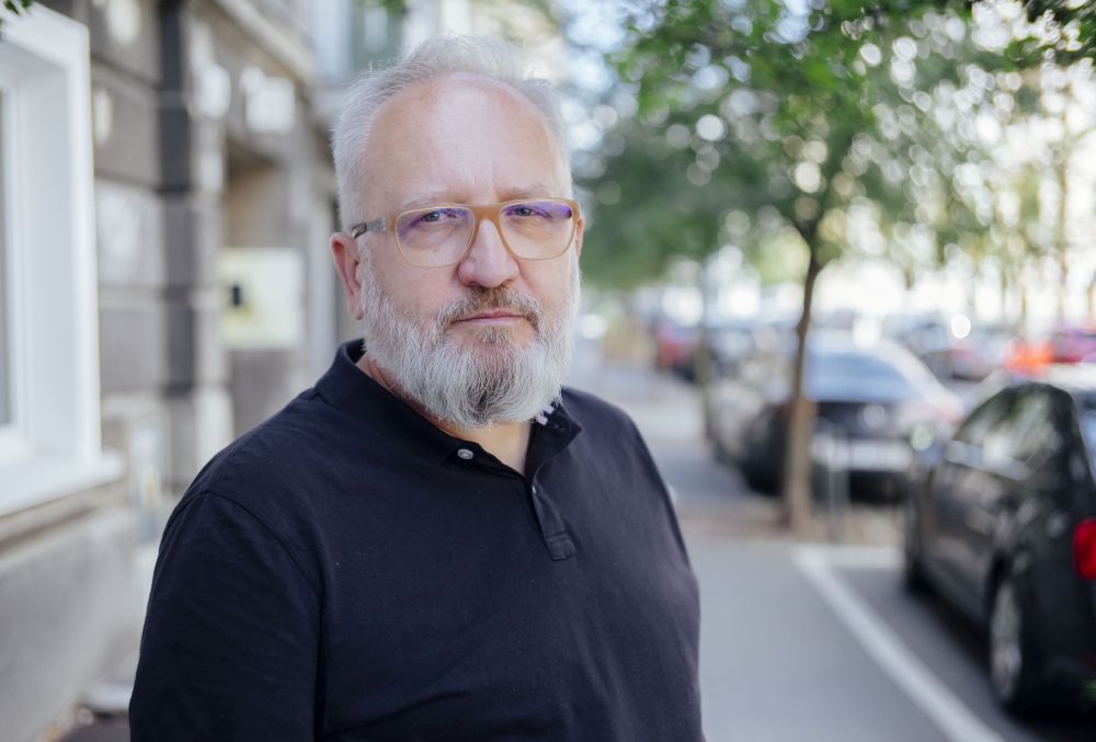 Brodaty mężczyzna w okularach stoi na ulicy.