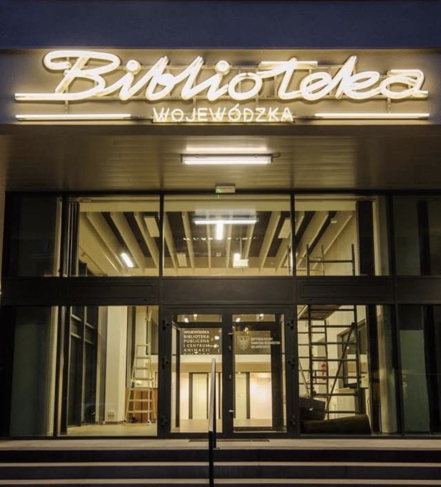 Budynek Biblioteki Wojewódzkiej nocą. Nad wejściem jasny neon.