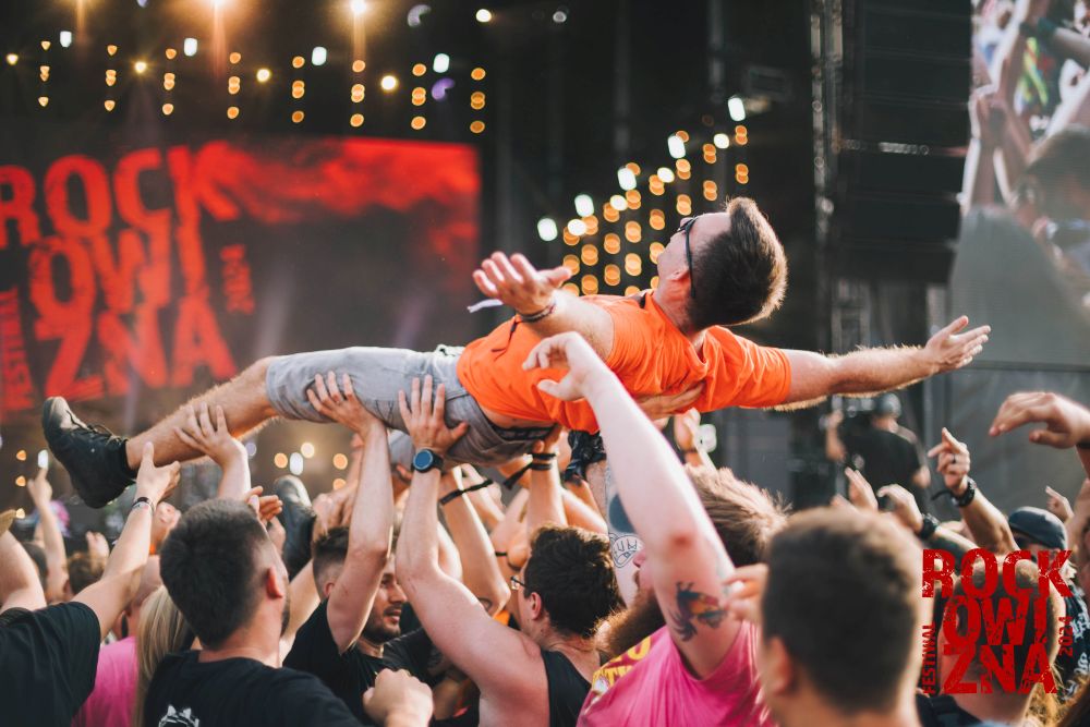 Chłopak w pomarańczowym T-shircie niesiony przez tłum na rękach.