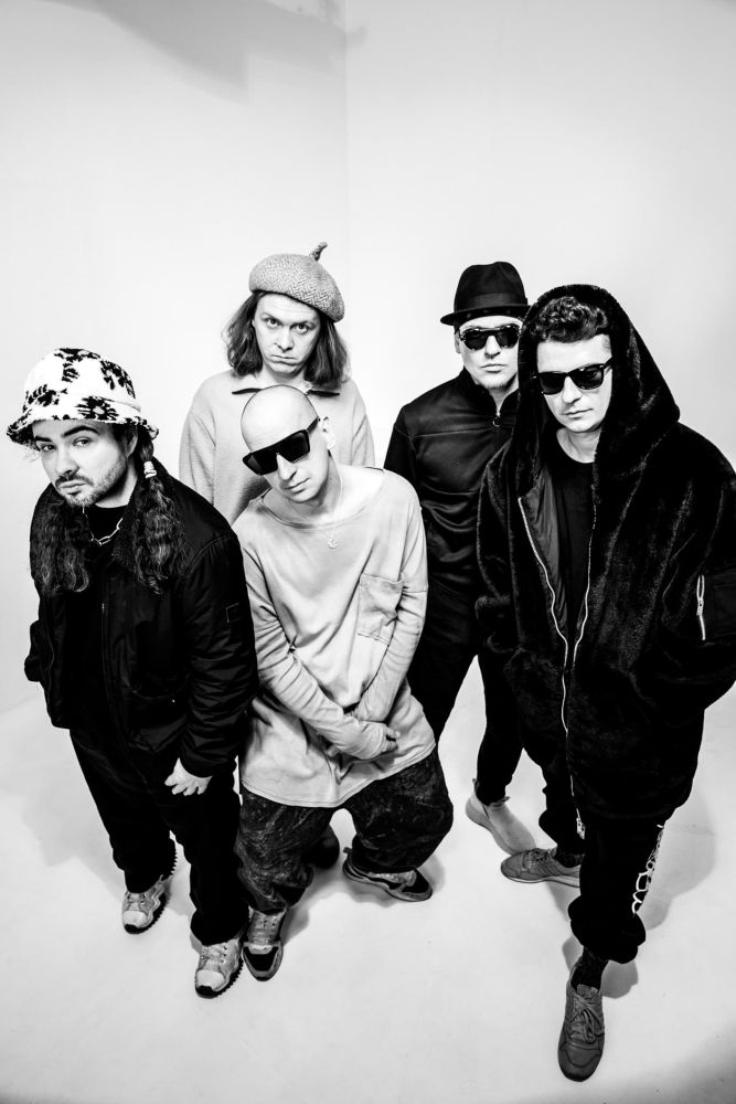 Członkowie zespołu spoglądają lekko w górę. Zdjęcie jest czarno-białe.