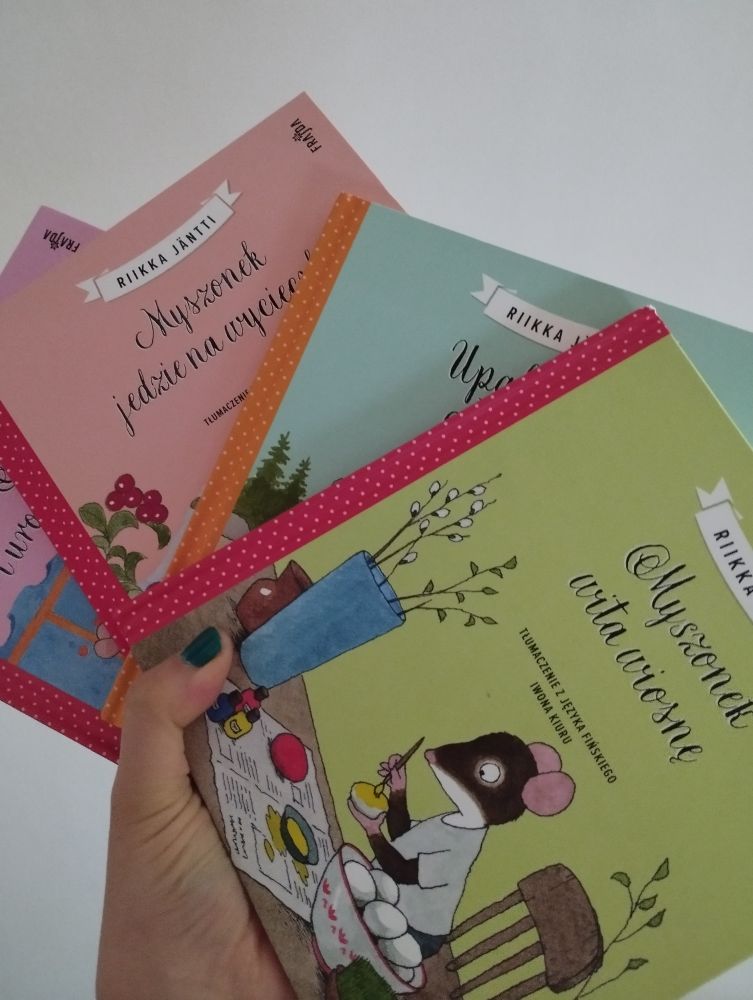 Cztery książki w jednej ręce, uformowane w wachlarz, by pokazać fragment każdej okładki.