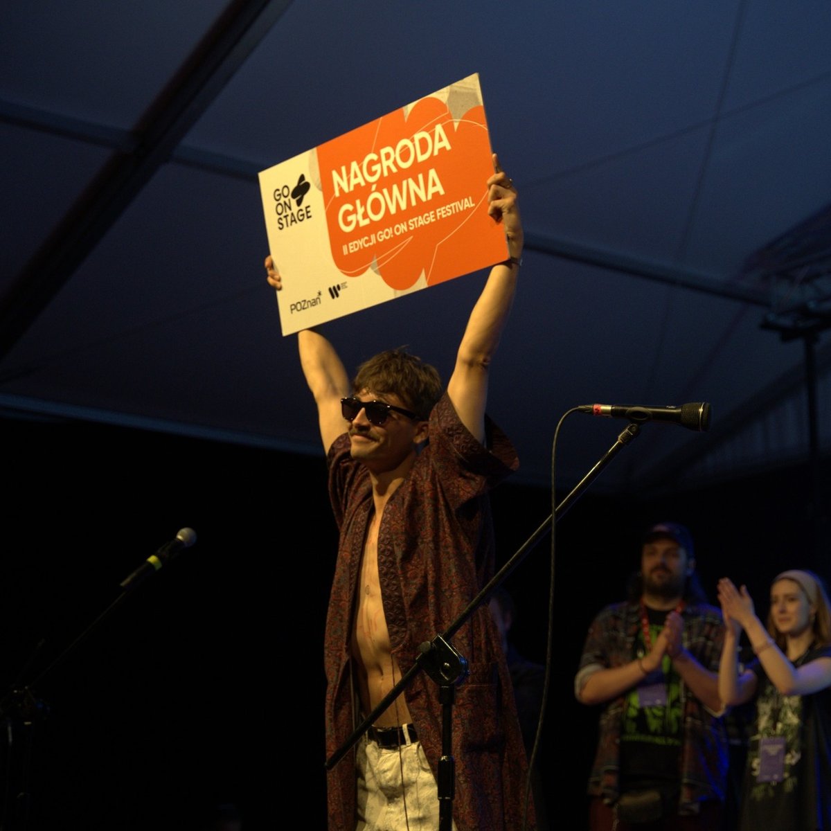 Dawid Tysowski podnoszący do góry tablicę z informacją o wygraniu Go On Stage Festival