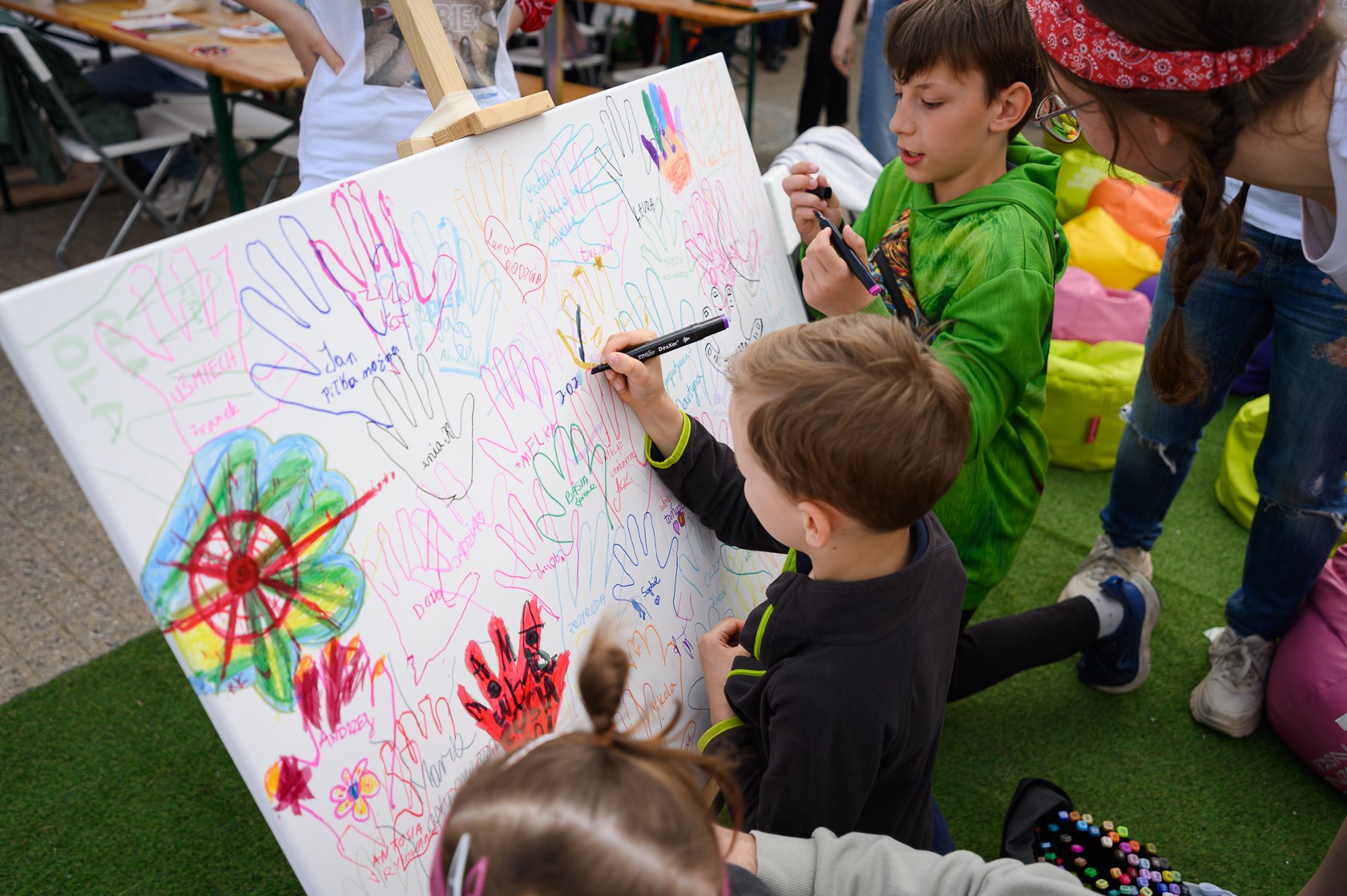 Dzieci stoją przed białą tablicą, na której każdy coś dorysowuje.