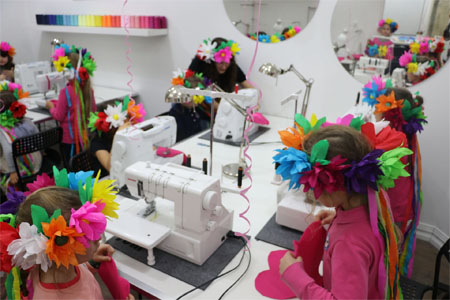 Foto:Dzieci w wiankach papierowych na głowach przy maszynach do szycia