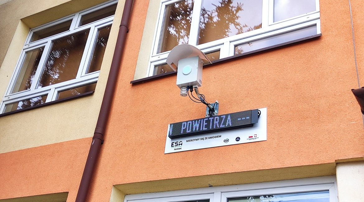 Fotografia przedstawia ścianę budynku z zamontowanym czujnikiem smogu