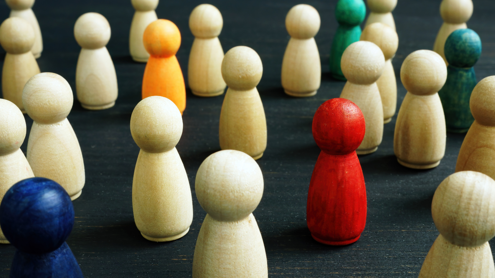 Grafika przedstawia czarne, drewniane podłoże, na którym rozstawione są drewniane pionki symbolizujące ogół społeczeństwa. Niektóre z tych pionków są kolorowe pośród pozostałych drewnianych - symbolika różnorodności.