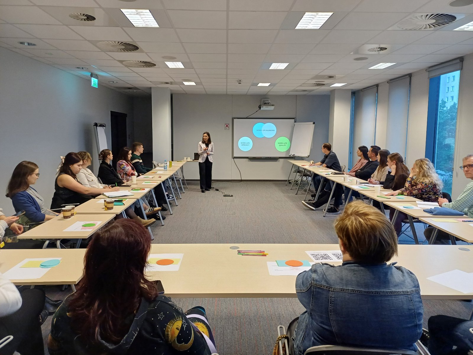 Grafika przedstawiająca zdjęcie ze szkolenia. Na zdjęciu są uczestnicy szkolenia stacjonarnego, którzy siedzą w sali szkoleniowej.