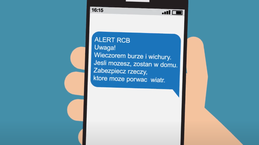 Grafika ręka trzyma telefon, na ekranie którego, wyświetla się informacja Alert RCB Uwaga! Wieczorem burze i wichury. Jesli możesz, zostań w domu. Zabezpiecz rzeczy, które może porwać wiatr.