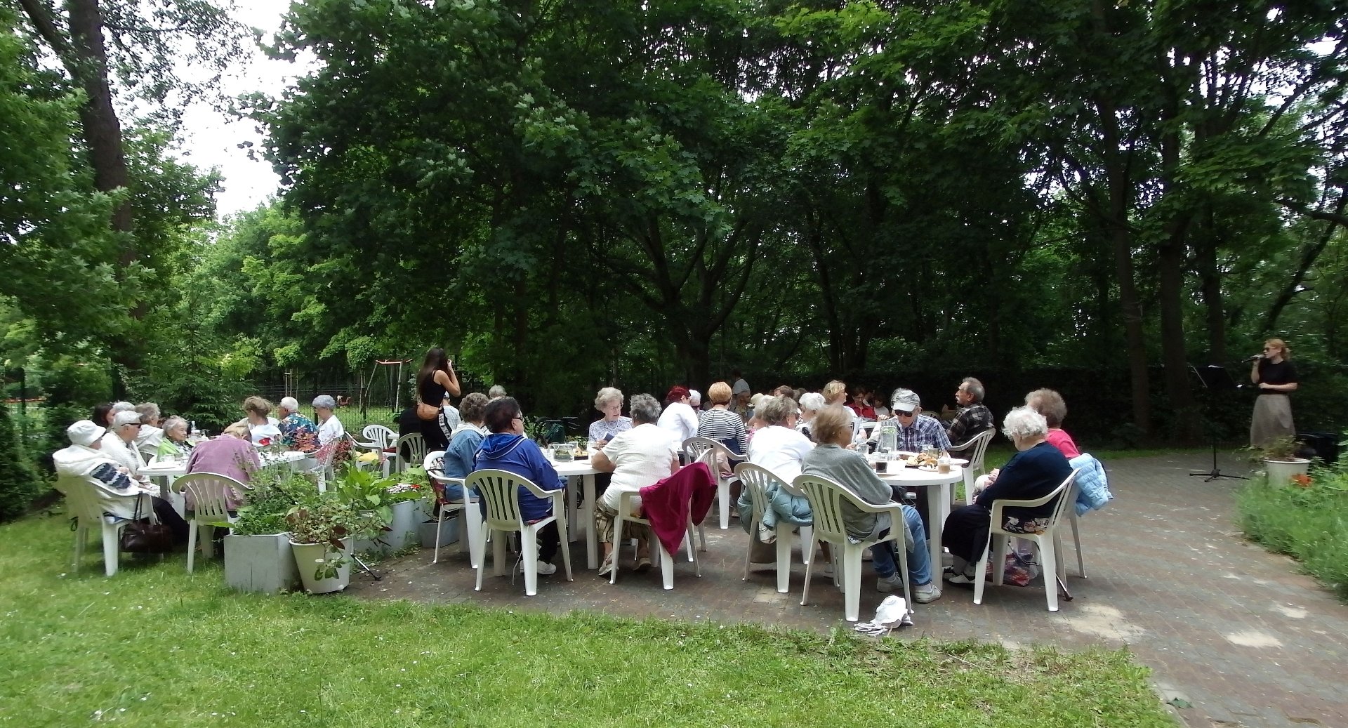 Grupa kilkudziesięciu osób przy stołach w ogrodzie