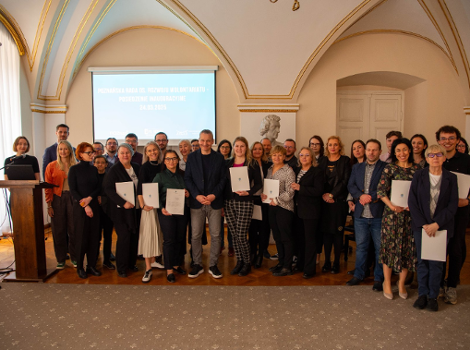 Poznań powołał Radę ds. Rozwoju Wolontariatu Grupa ludzi w eleganckim wnętrzu z łukowym sufitem i bogatymi dekoracjami. Osoby pozują do zdjęcia przed ekranem z napisem: ,POZNAŃSKA RADA DS. ROZWOJU WOLONTARIATU - POSIEDZENIE INAUGURACYJNE 24.03.2025'. Po lewej stronie podium z mikrofonem. Część osób trzyma certyfikaty lub dokumenty.