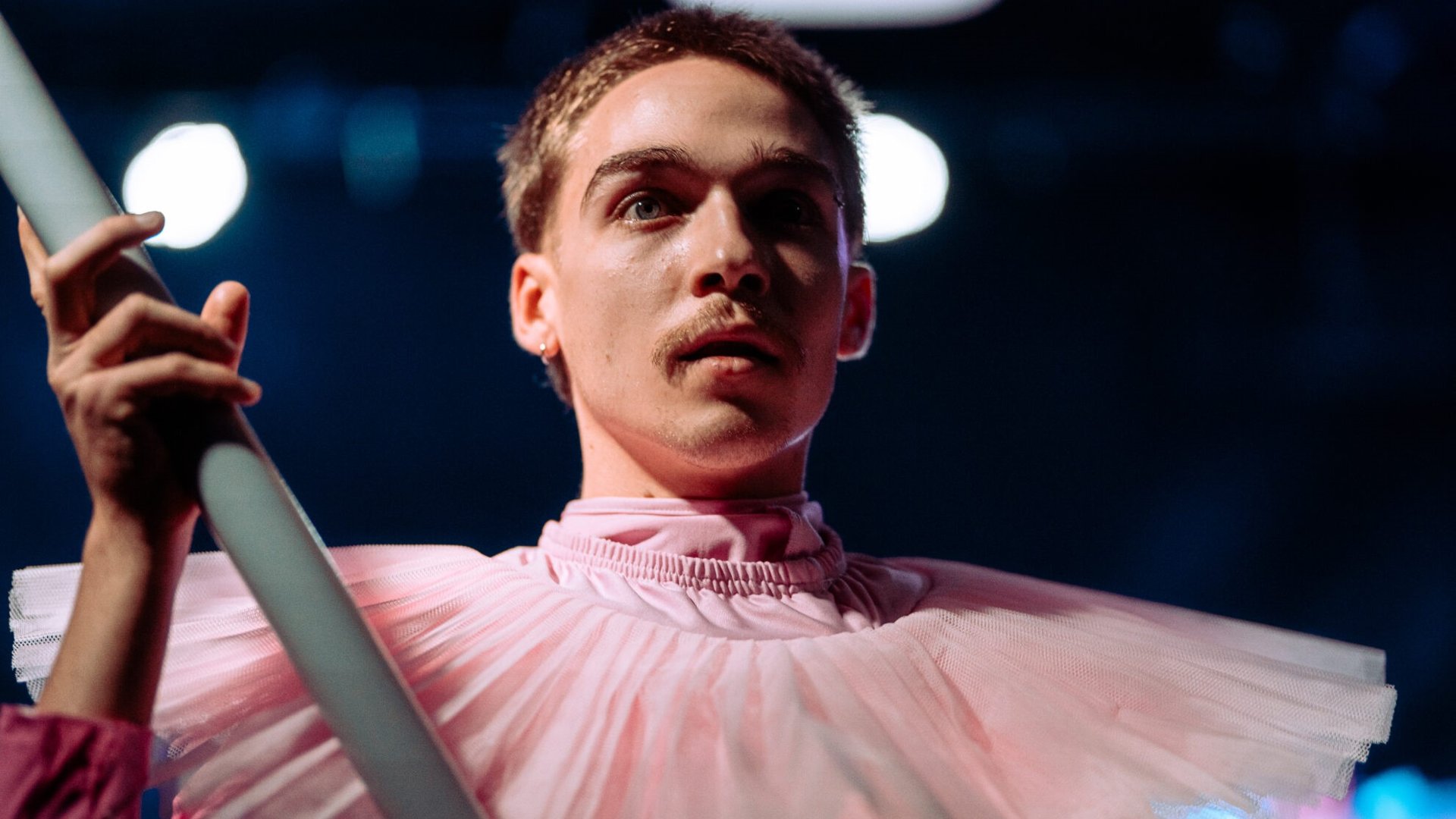 Zdjęcię mężczyzny w różowym stroju, który trzyma szary rurę.