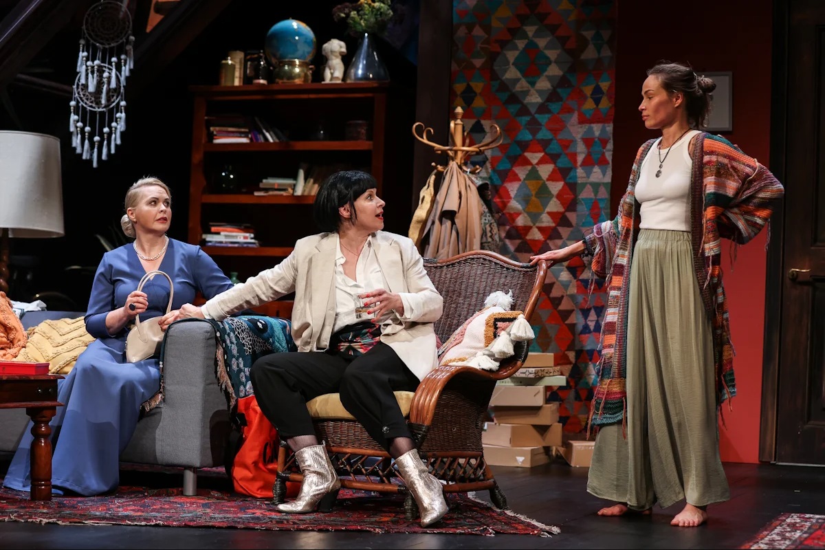 Kadr ze spektaklu - dwie kobiety patrzą na siebie, stojąc przy zastawionym przedmiotami blacie