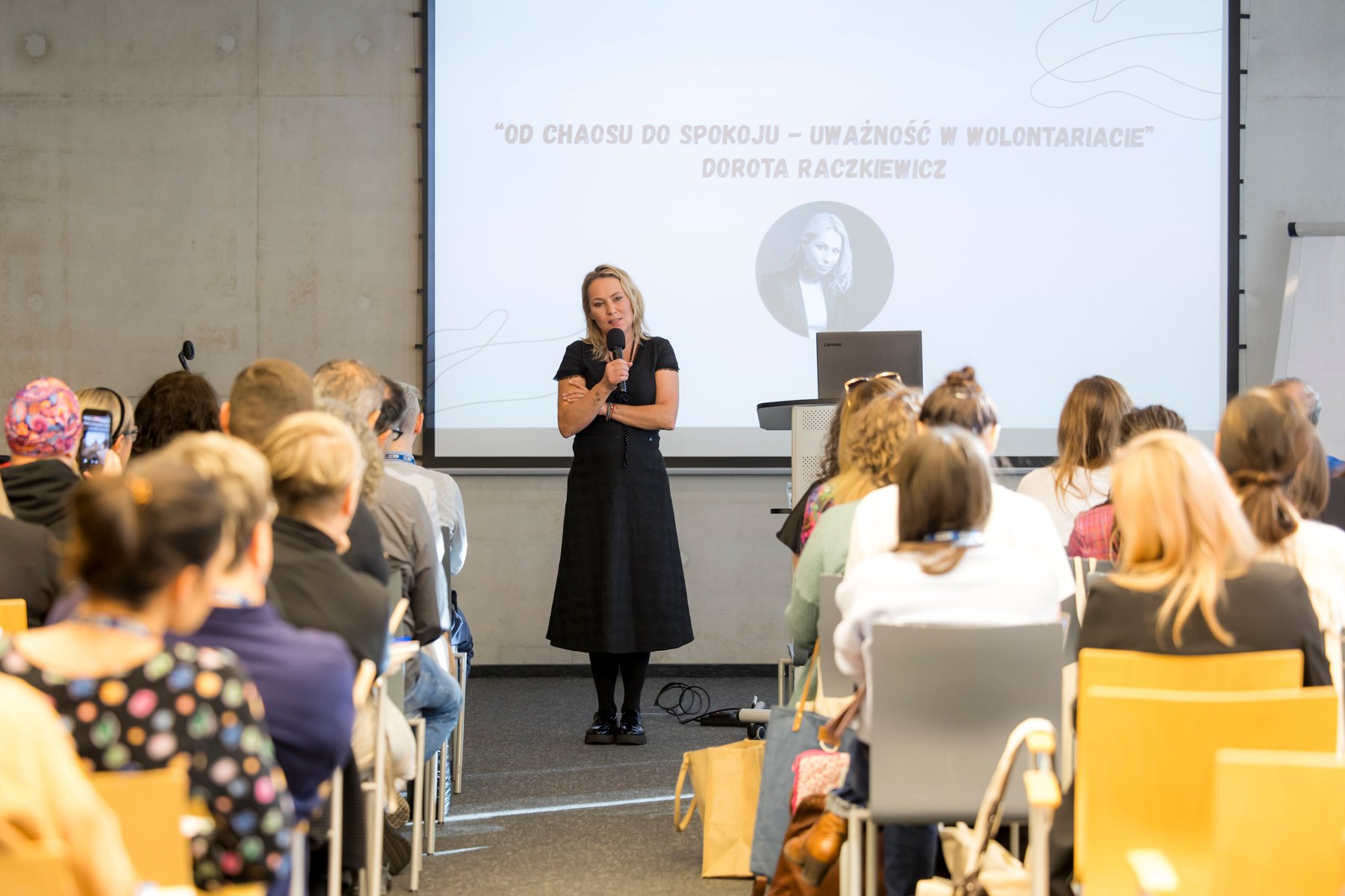 Kobieta z mikrofonem przemawiam do uczestników Forum, w tle prezentacja z tytułem wystąpienie i zdjęciem