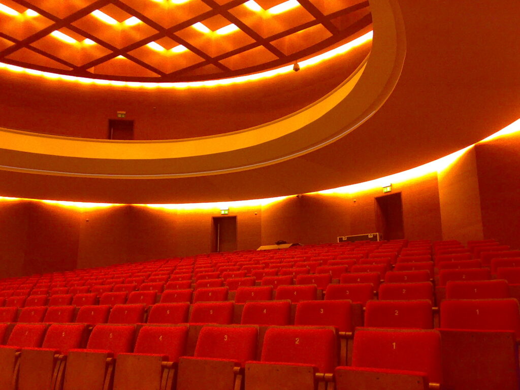 Obrazek przedstawia aule z czerwonymi krzesłami.