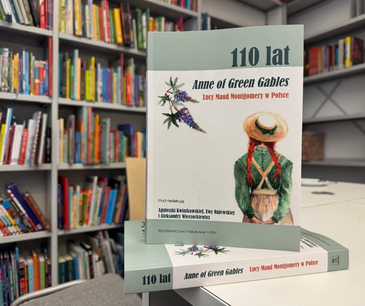 Książka stoi na białym biurku, za nią regały zapełnione innymi książkami.