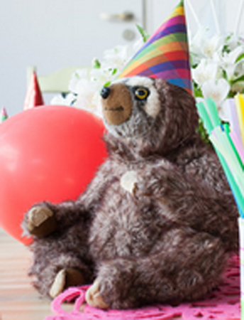 Leniwiec w kolorowej czapeczce obok czerwony balonik.