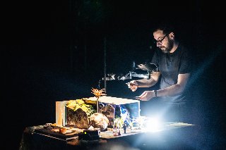 Mężczyzna pochyla się nad oświetloną makietą.