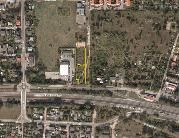 Mapa satelitarna terenu miejskiego z naniesionymi nazwami ulic (m.in. Jana Henryka Dąbrowskiego, Santocka, Zygmunta Żuraszka). W centrum znajduje się wąska, prostokątna działka oznaczona żółtym obrysem z symbolem »1MW/U«. Wokół widoczna jest zabudowa jednorodzinna, ogrody działkowe oraz wielopasmowa arteria komunikacyjna w dolnej części obrazu. W prawym dolnym rogu umieszczono podziałkę liniową 0-100 m.