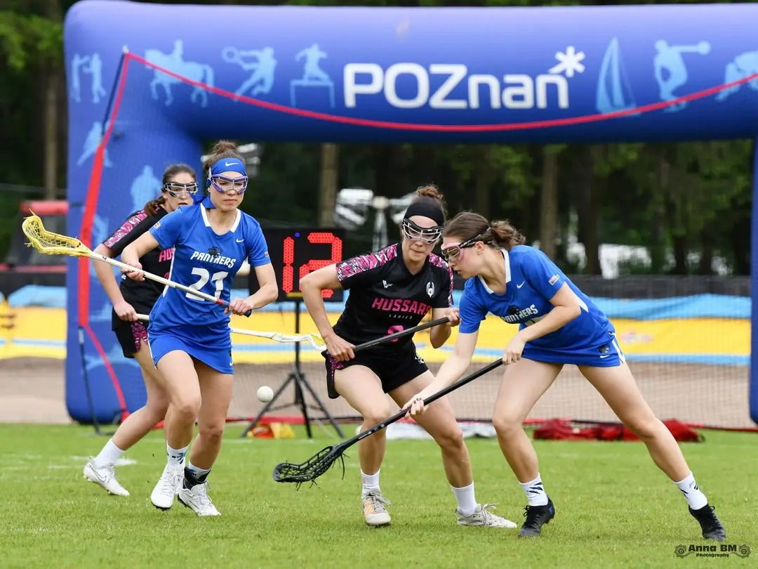 Mecz zespołu Poznań Hussars Ladies, fot. Anna BM Photography - po 2 zawodniczki w niebieskich i czarno-różowych strojach, zaś w tle brama pneumatyczna Poznania