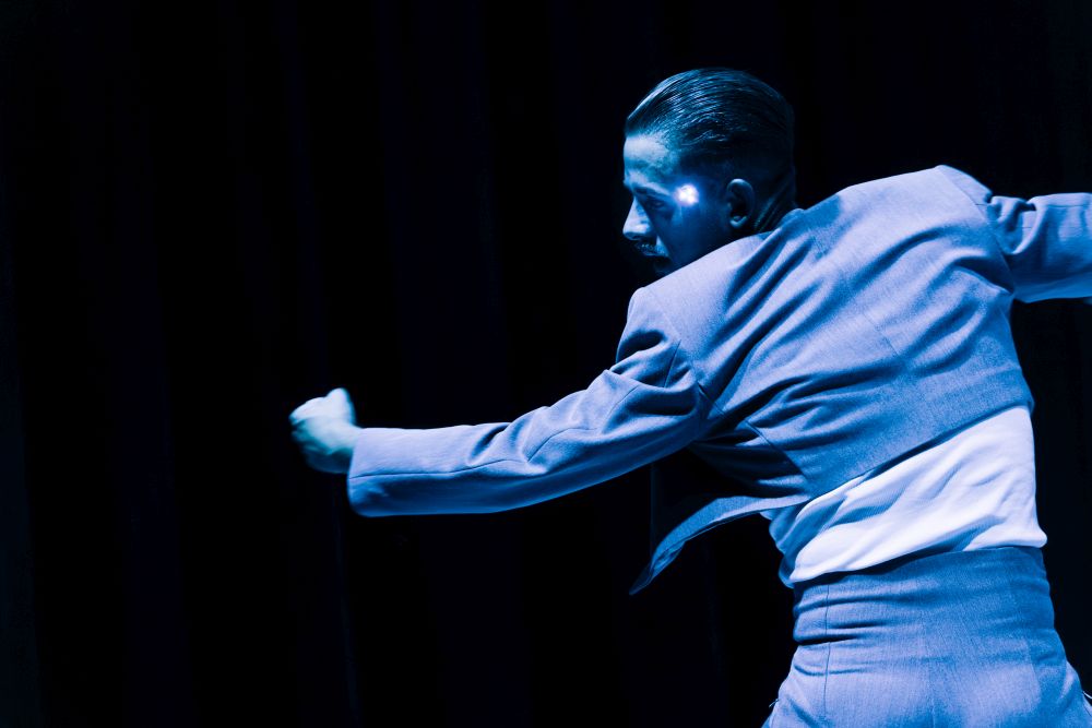 Mężczyzna tańczy w ciemności. Widzimy jego twarz z profilu, na skroni ma palące się światełko.