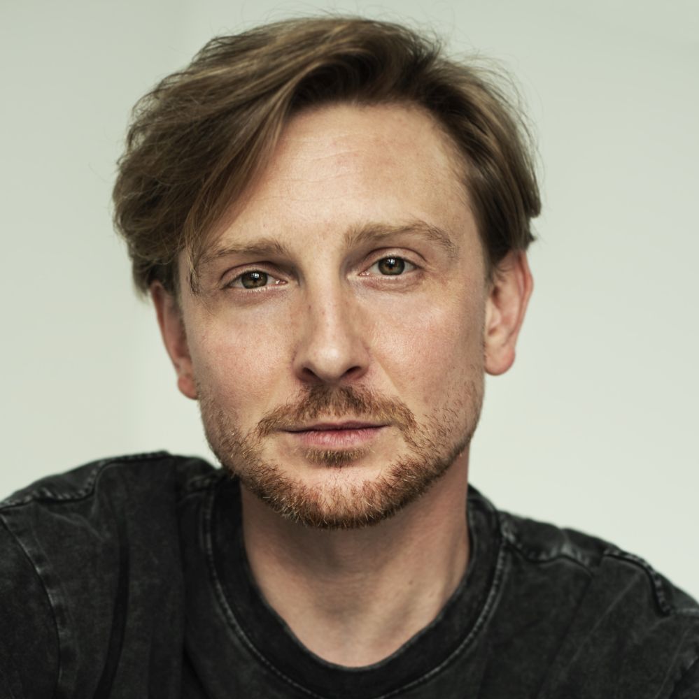 Mężczyzna w czarnym T-shircie patrzy prosto w obiektyw.