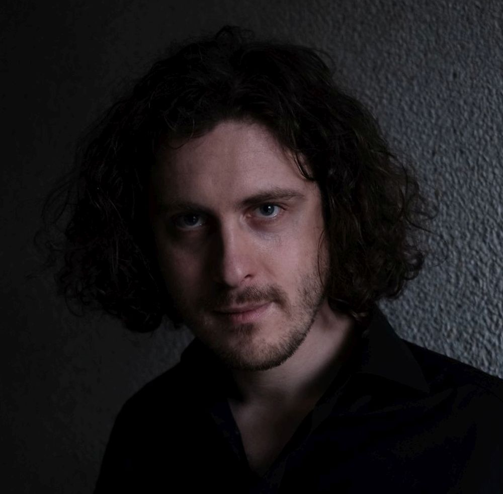 Mężczyzna w długich włosach patrzy w obiektyw.