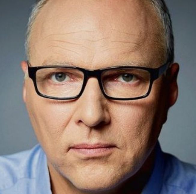 Mężczyzna w średnim wieku, z poważnym wyrazem twarzy, w okularach.