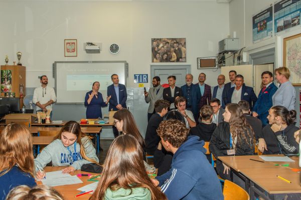 Na grafice przedstawiono grupę ludzi uczestniczących w Szkolnym Dniu Przedsiębiorczości.