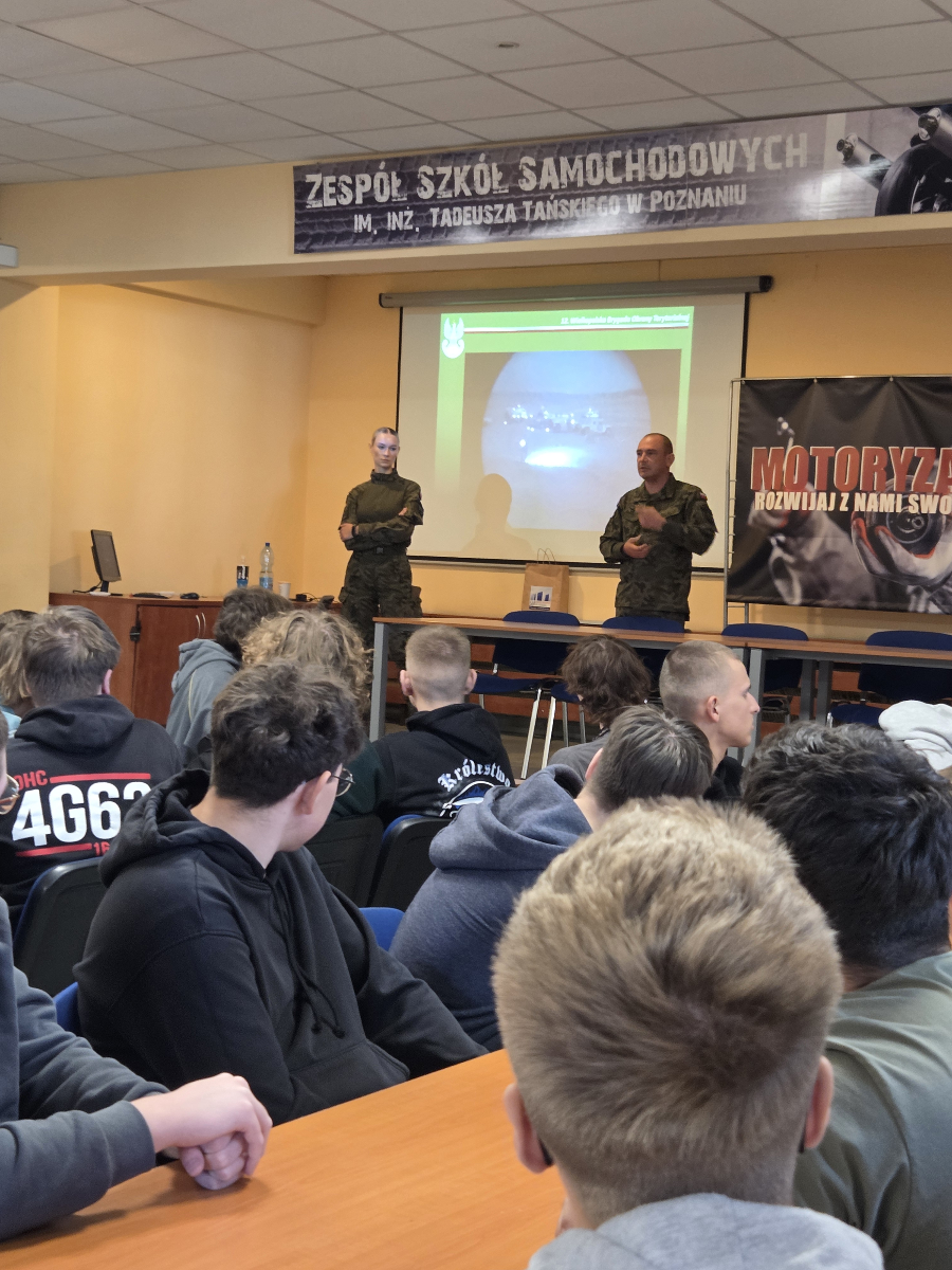 Na grafice znajdują się uczniowie siedzący w klasie i oglądający prezentację multimedialną