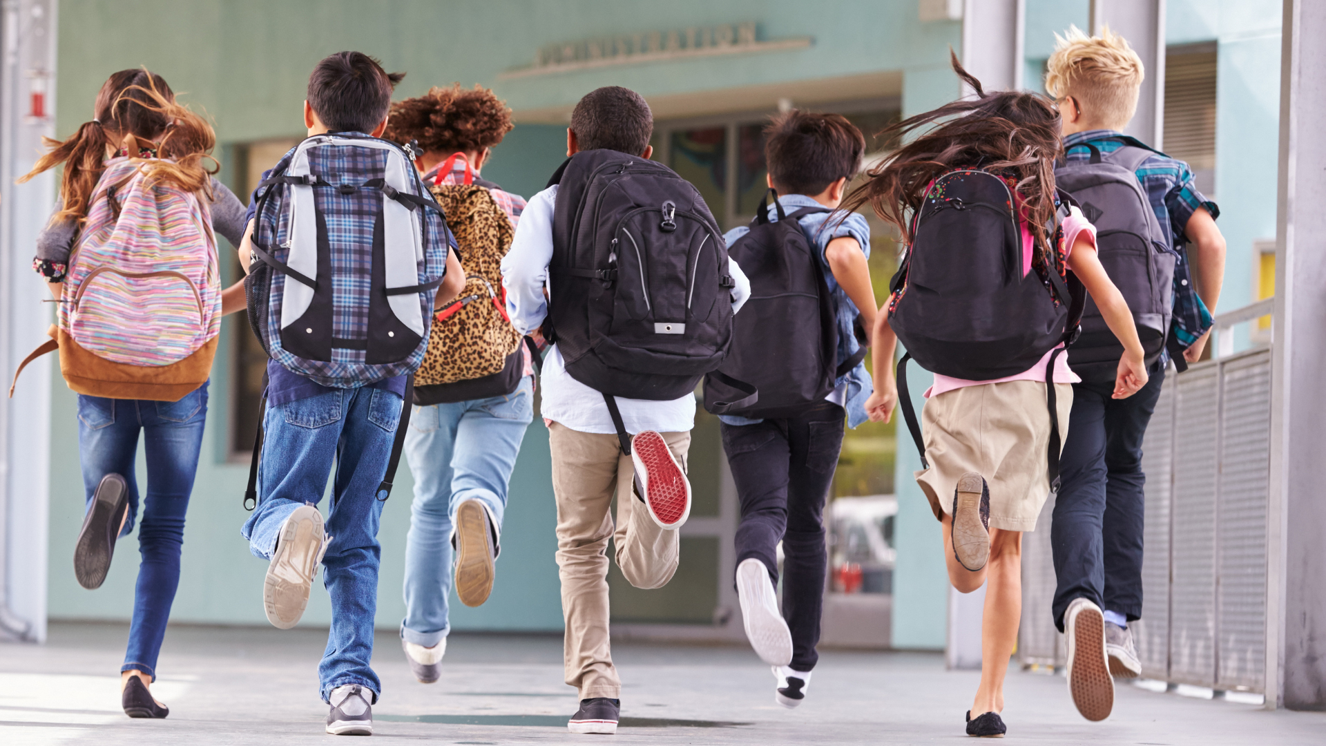 na obrazku dzieci na korytarzu szkolnym, pokazane tyłem, z plecakami na plecach, biegnące na zajęcia szkolne