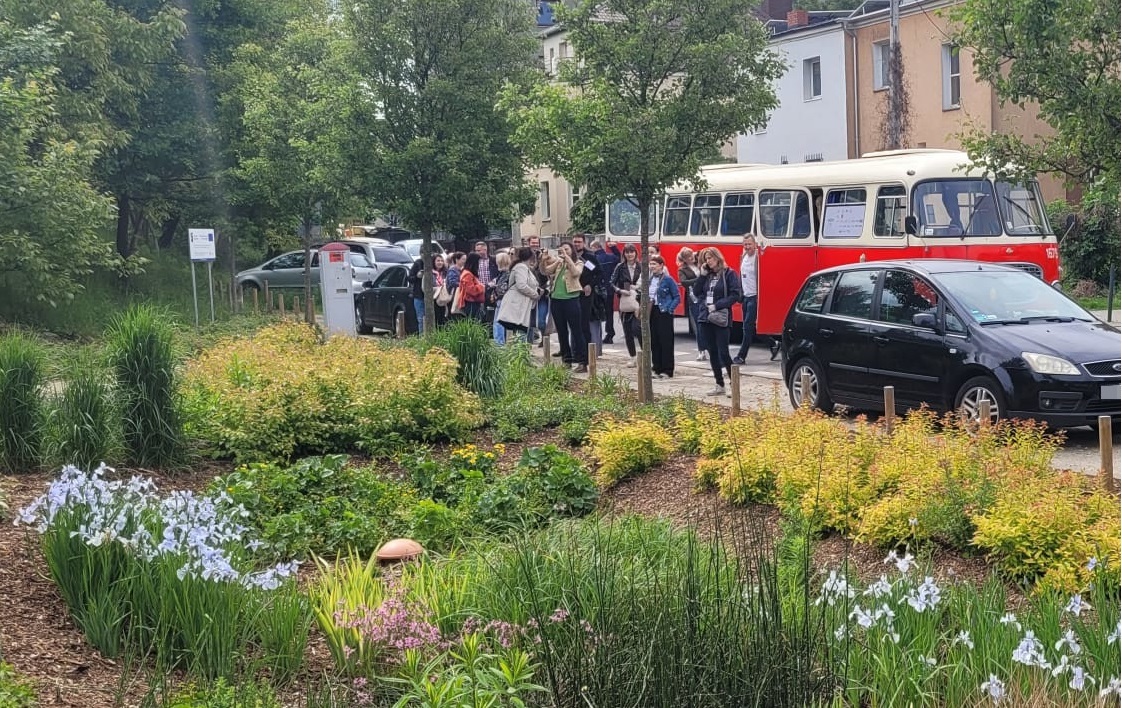 Na podświetlonej podłodze siedzi grupa dzieci i słucha prowadzącej zajęcia. Wokół stoją opiekunowie.