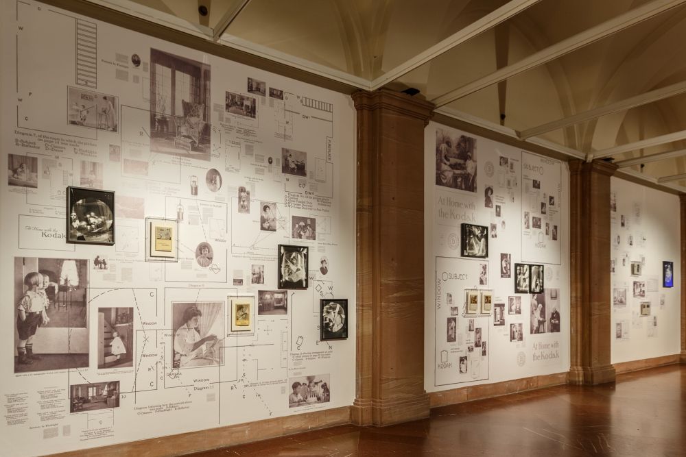 Na ścianie podświetlonej ostrymi światłami - czerwonym, zielonym, niebieskim, jest półka z trzema fotografiami, pozornie do siebie podobnymi. Patrzą na nie trzy zwiedzające.