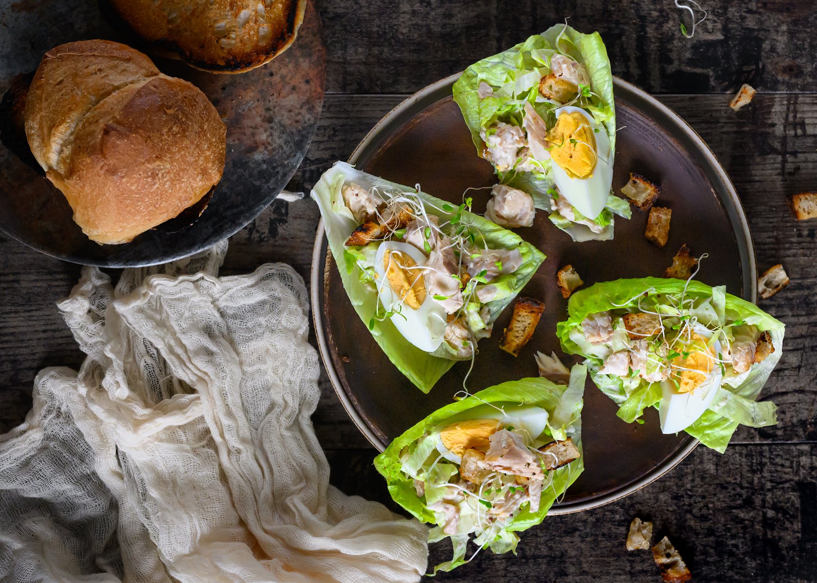 Na talerzu liście sałaty, a na nich kawałki jajka, pstrąga, grzanki z pieczywa, posypane kiełkami.