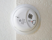 Na zdjęciu biała, okrągła czujka przymocowana do białej ściany