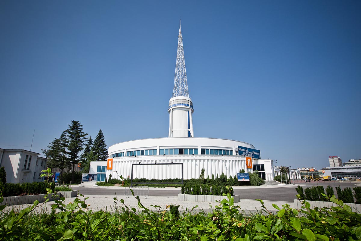 Na zdjęciu budynek Iglicy na Międzynarodowych Targach Poznańskich, widać okrągłą formę budynku i jego wysoką wieżę