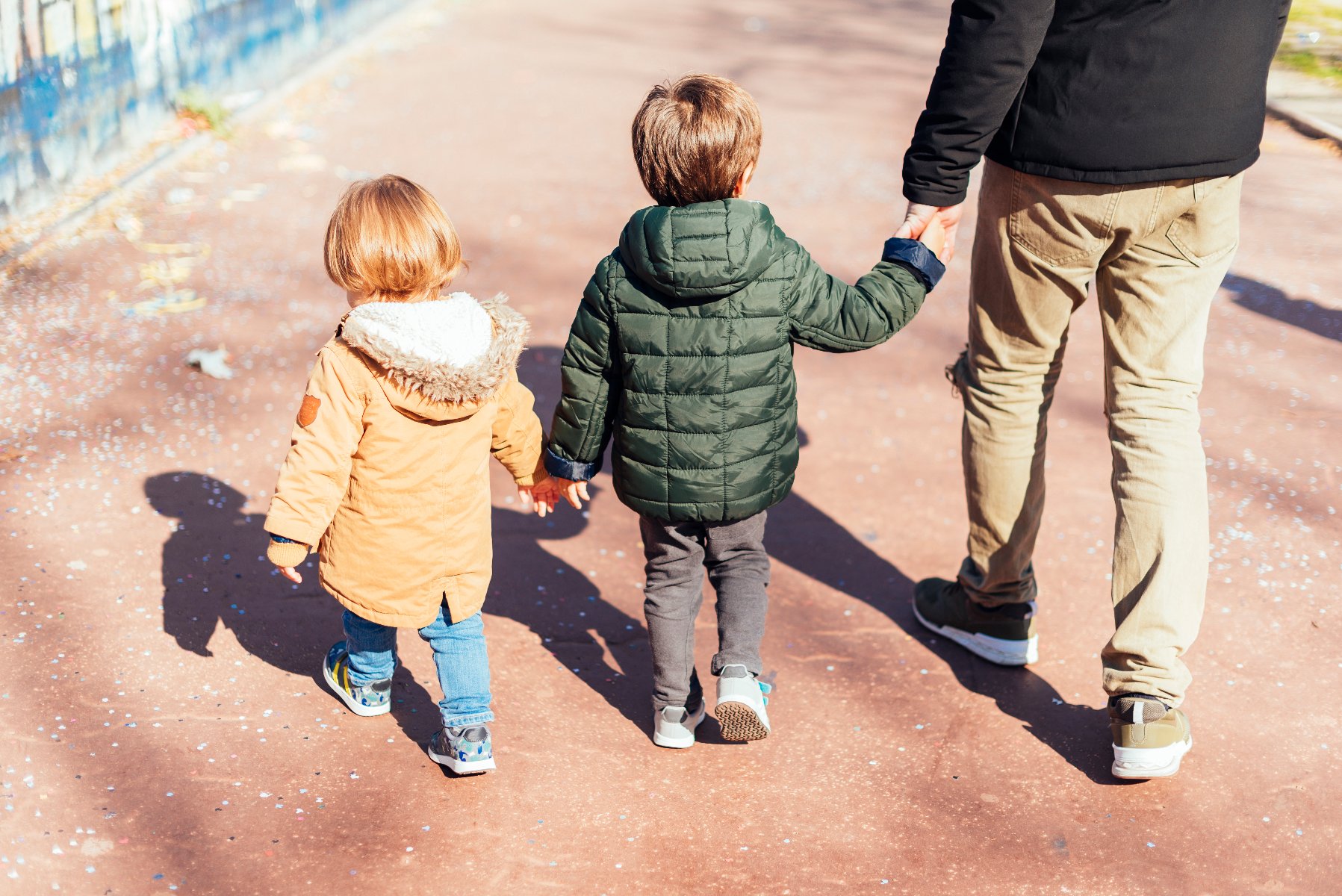 Na zdjęciu dorosły z dwójką dzieci na parkowej ścieżce, wszyscy są odwróceni tyłem do obiektywu