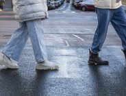 Na zdjęciu dwie osoby przechodzące przez przejście na pasach na wilgotnej jezdni, widać tylko ich nogi