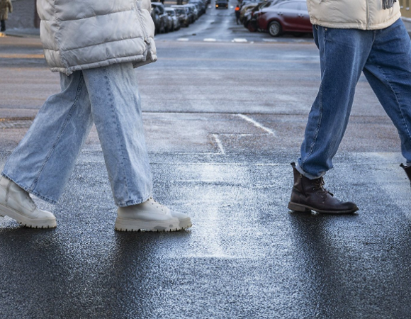 Na zdjęciu dwie osoby przechodzące przez przejście na pasach na wilgotnej jezdni, widać tylko ich nogi