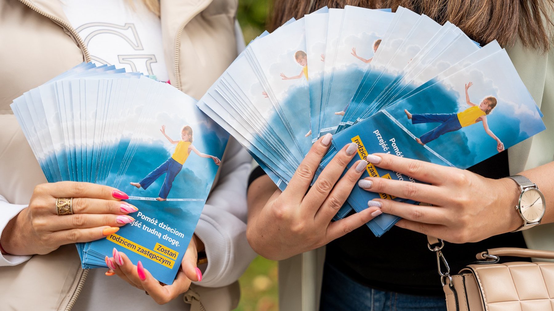 Na zdjęciu dwie osoby trzymające ulotki z napisem: pomóż dzieciom przejść trudną drogę
