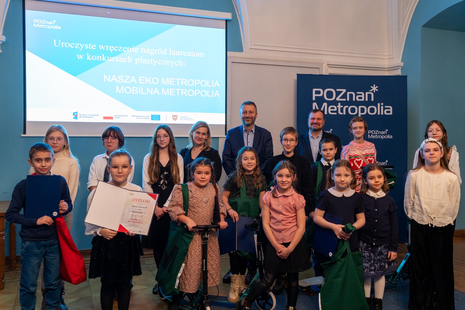 Na zdjęciu dziecko w korytarzu urzędu, jedzie na hulajnodze, obok widać prace plastyczne na sztalugach